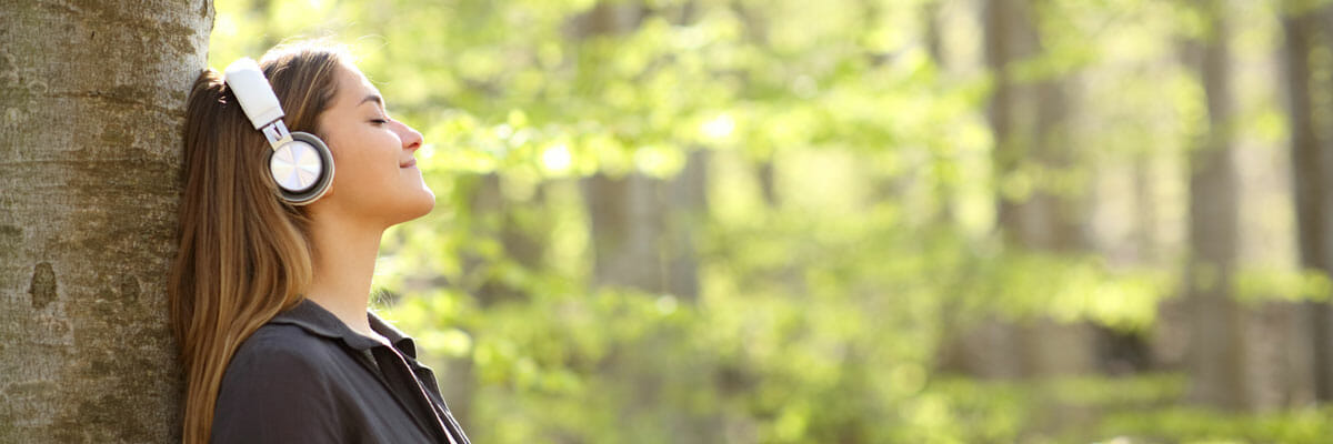 Woman listens to music as she sits against a tree | Pacific Arboriculture